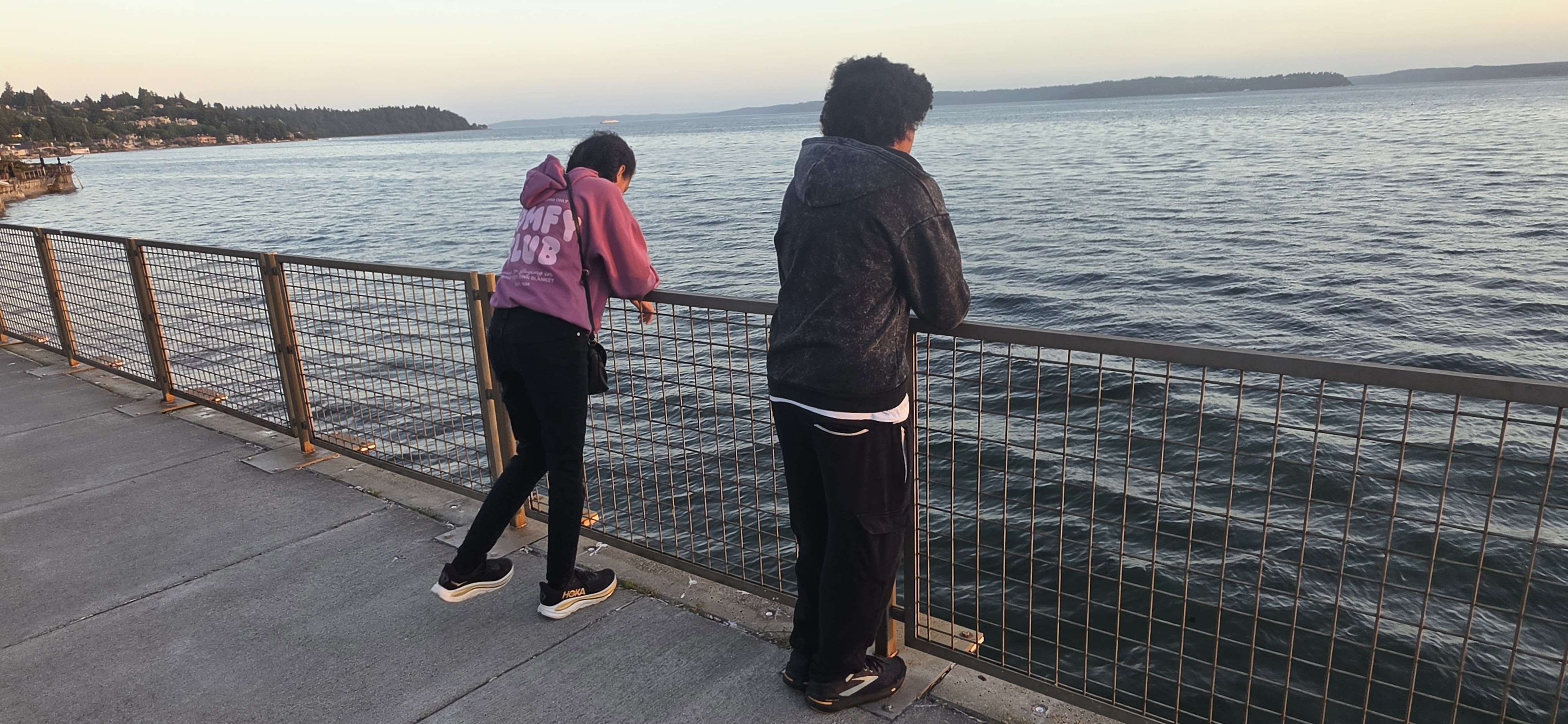 Two kids standing on a pier, looking out over the water