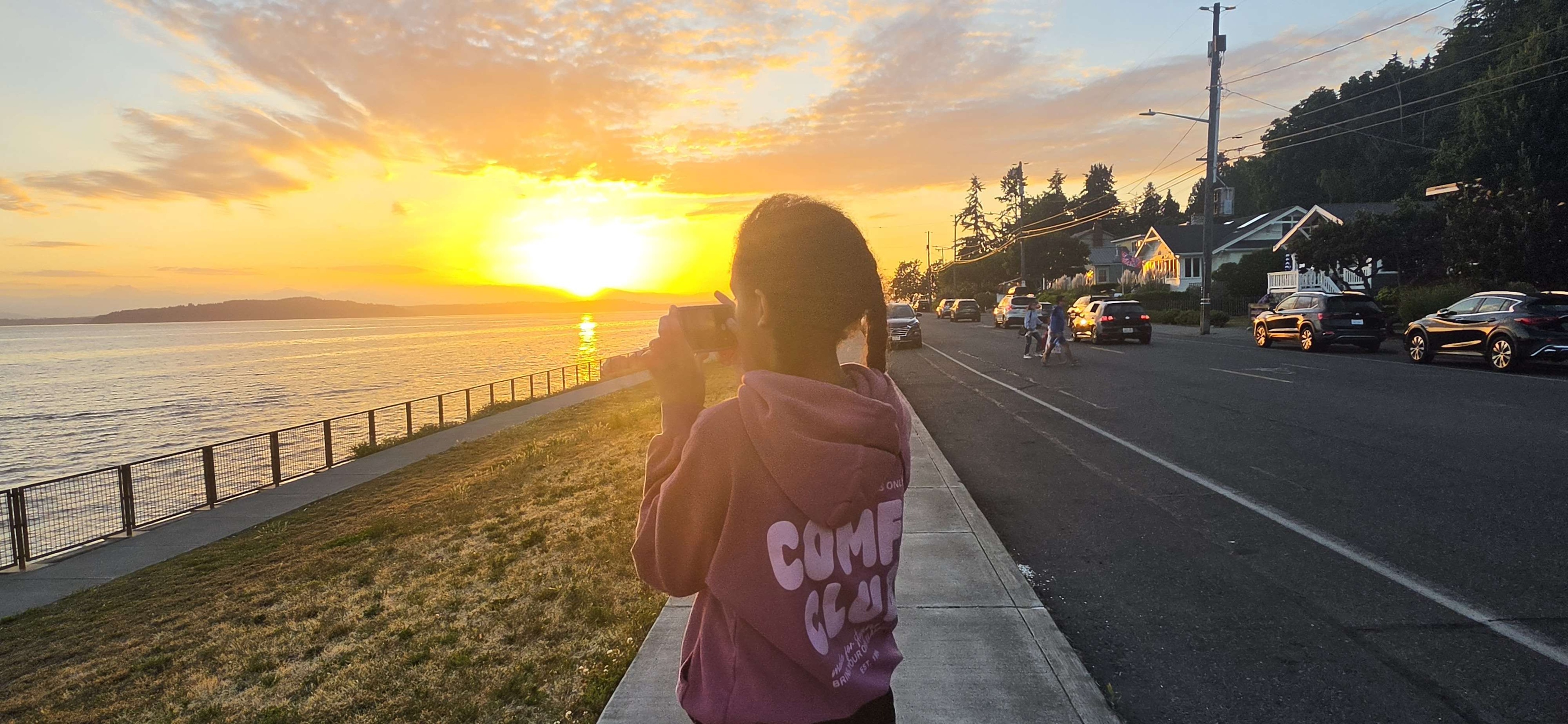 A kid from behind, photographing the sunset over the water